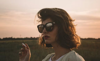 a woman in glasses smoking at dusk